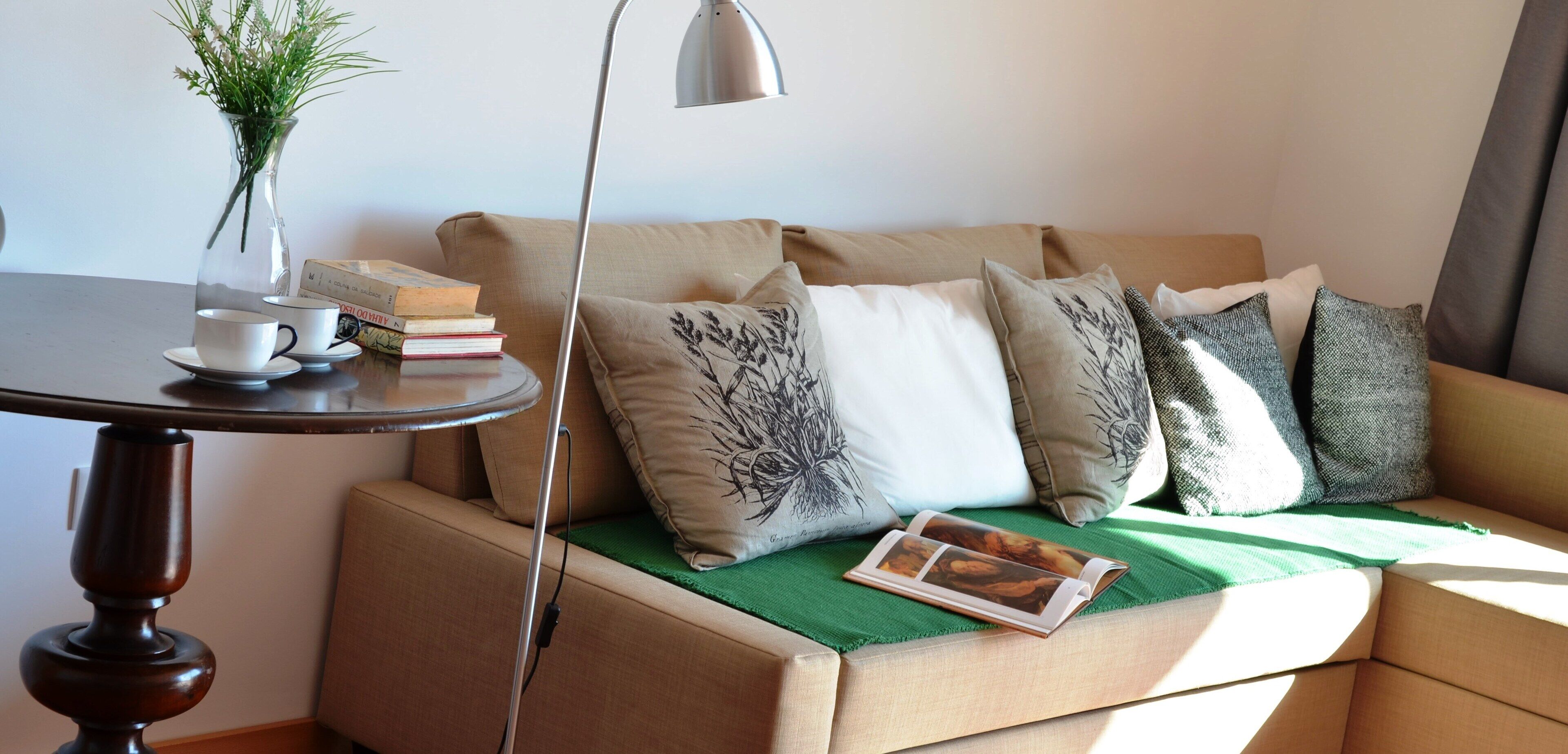 Un rincón acogedor con un sofá, una mesa con un florero y libros, y una lámpara.