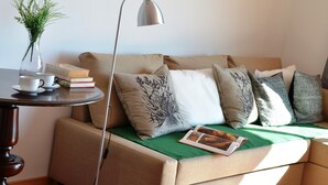 A cozy living area with a sofa, a table with a vase and books, and a lamp. - Funchal Carvalhal Old Town (Funchal)