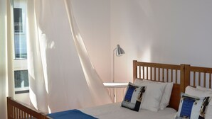 A bedroom with a wooden bed, a blue bedspread, white pillows, and a white lamp on a bedside table. - Funchal Carvalhal Old Town (Funchal)