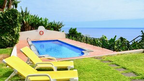 A swimming pool with a view of the ocean, surrounded by greenery and yellow lounge chairs. - Esmee Apartment, Big Terrace with Sea View! (Arco Da Calheta)