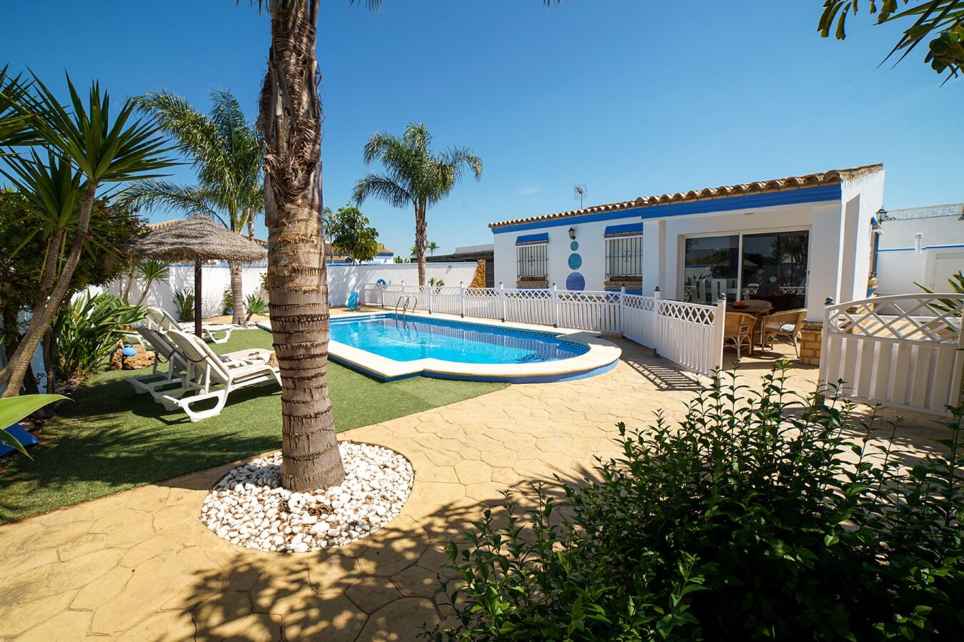 Une piscine entourée d’une clôture blanche, avec une maison en arrière-plan.