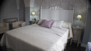 Habitación de hotel con una cama grande, dos mesitas de noche con lámparas, una silla y un cabecero decorativo.