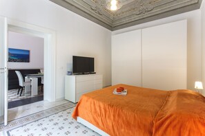 Une chambre d’hôtel avec un lit, un téléviseur posé sur une commode blanche, un bureau avec une chaise et un tableau accroché au mur.