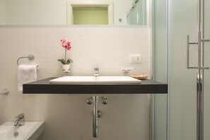 Une salle de bain avec un lavabo blanc, un porte-serviettes, une orchidée en pot et une cabine de douche en verre.