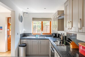 A modern kitchen with a built-in oven, a sink, and a window with a view of greenery. - Monmouth Cottage - A peaceful, rural cottage retreat on the outskirts of Frome, near Longleat Safari (Beckington)