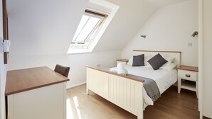Une chambre avec un plafond en pente, un puits de lumière, un lit avec des oreillers, une table de chevet et un bureau.