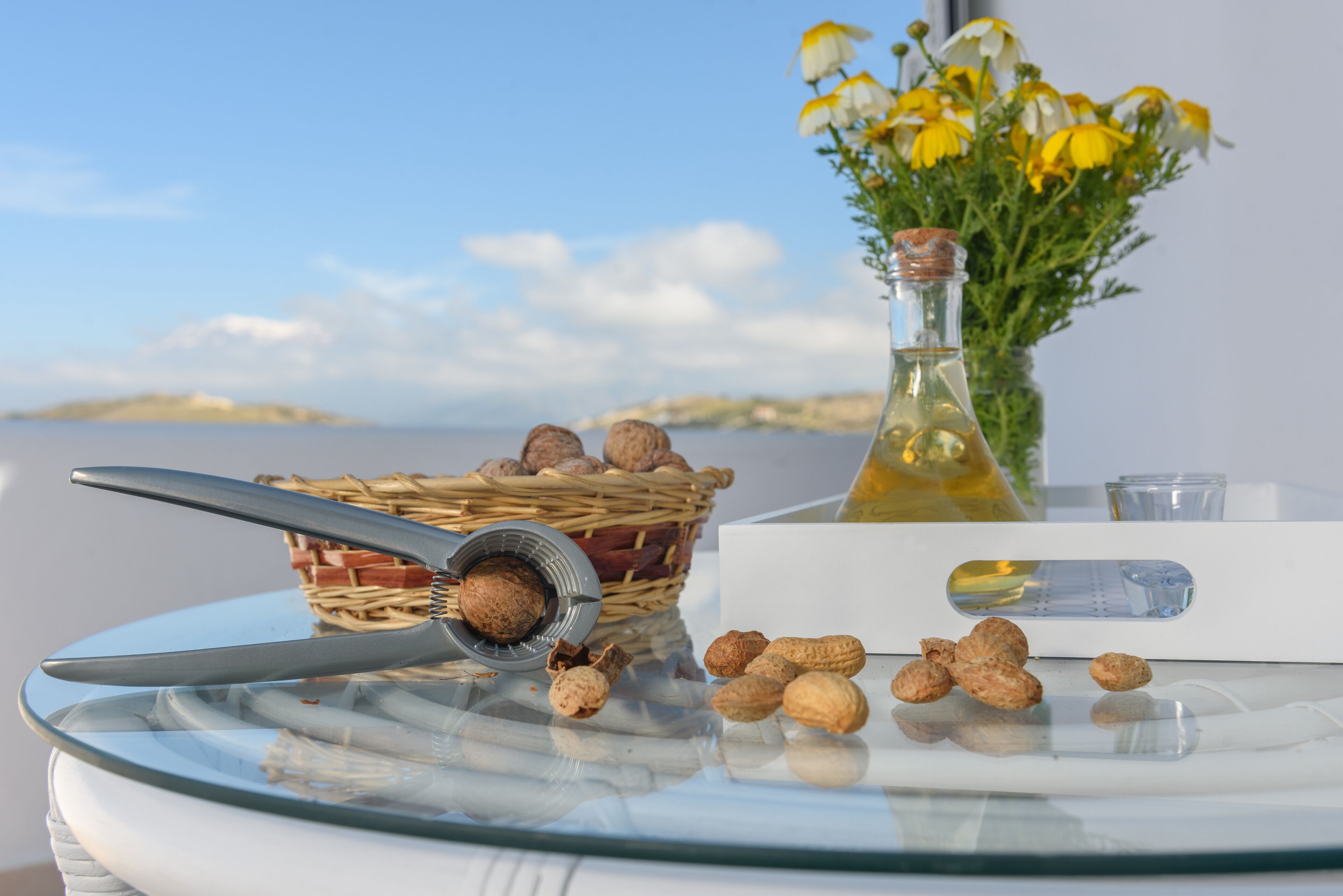 Une table sur laquelle se trouve un saladier en verre rempli de fruits secs, un panier en osier, une bouteille d’huile et un vase avec des fleurs.