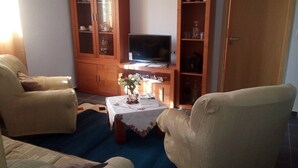 A living room with two beige armchairs, a wooden cabinet with glass doors, a television, and a small table with a vase of flowers. - Calm and rest combined with well-being with great views of the mountain and sea (Madalena)