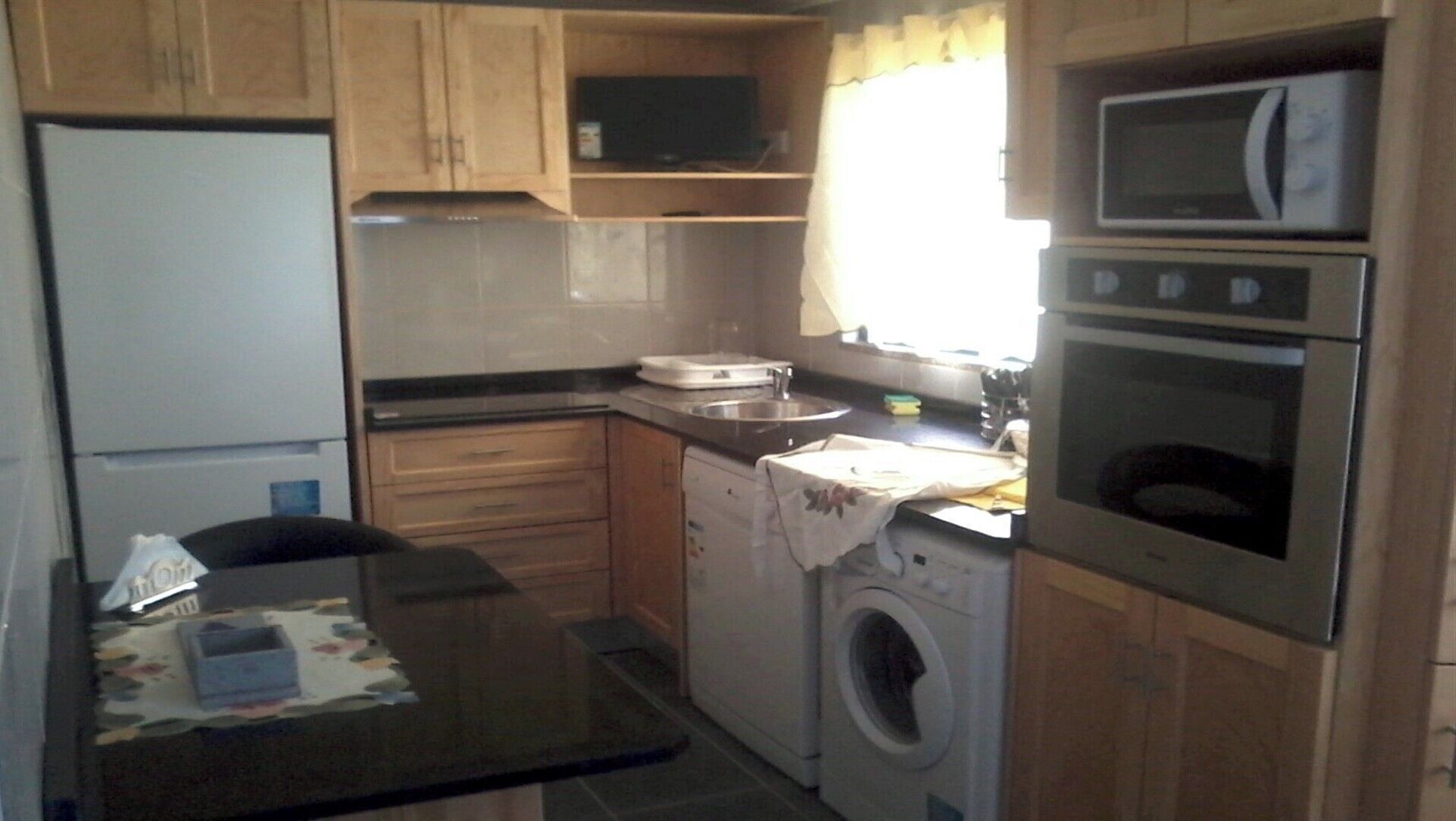 A compact kitchen with wooden cabinets, a microwave, an oven, a sink, and a washing machine.