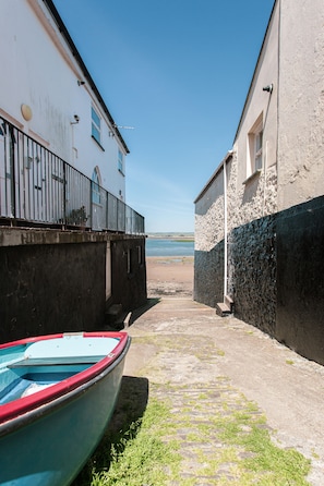 Un étroit sentier pavé de pierres menant à une plage, avec un bateau et des bâtiments de chaque côté.
