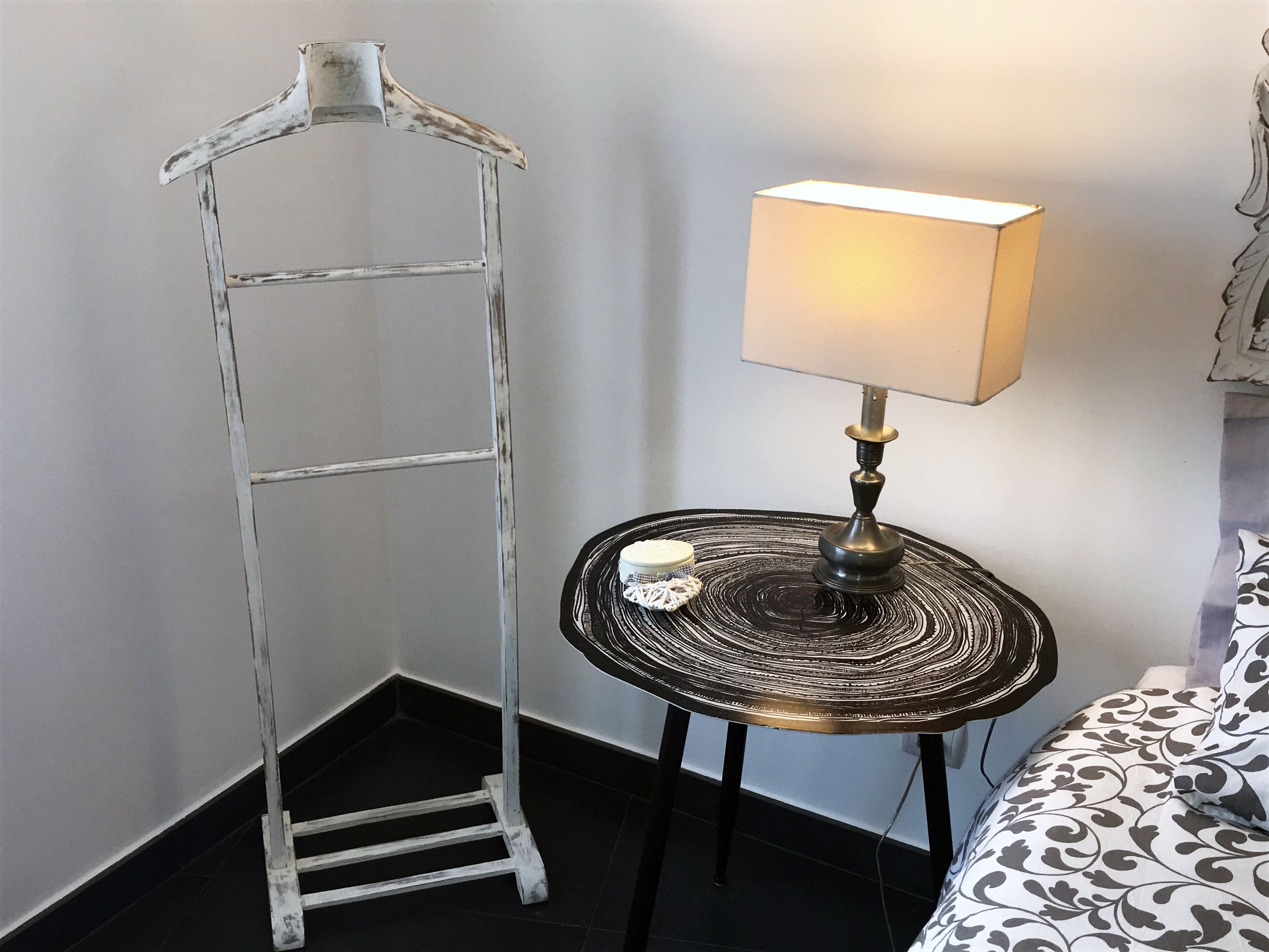 A room with a metal drying rack, a table with a lamp, and patterned bedding.