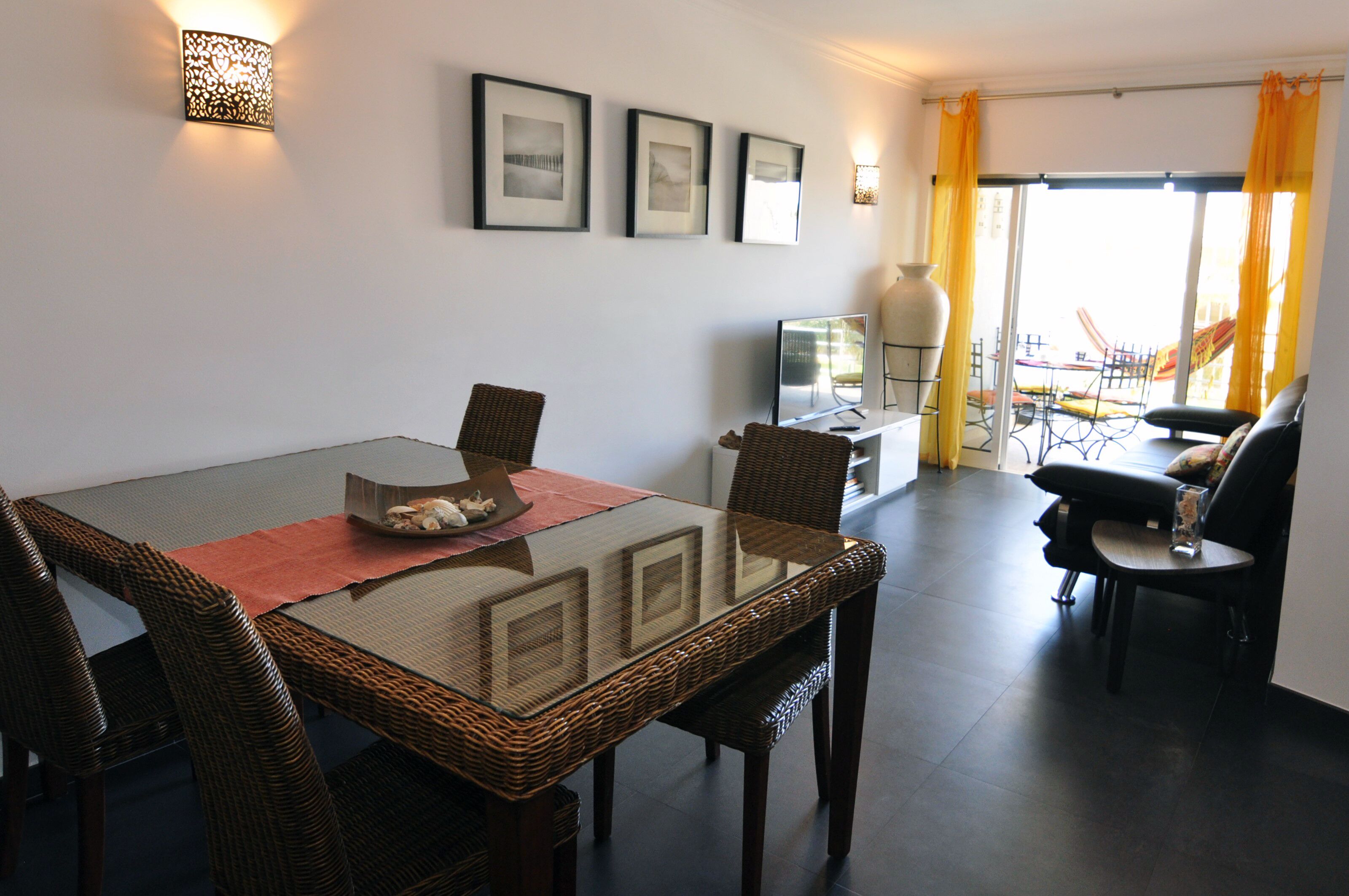 A dining area with a glass-top table, wicker chairs, and a TV on a stand.