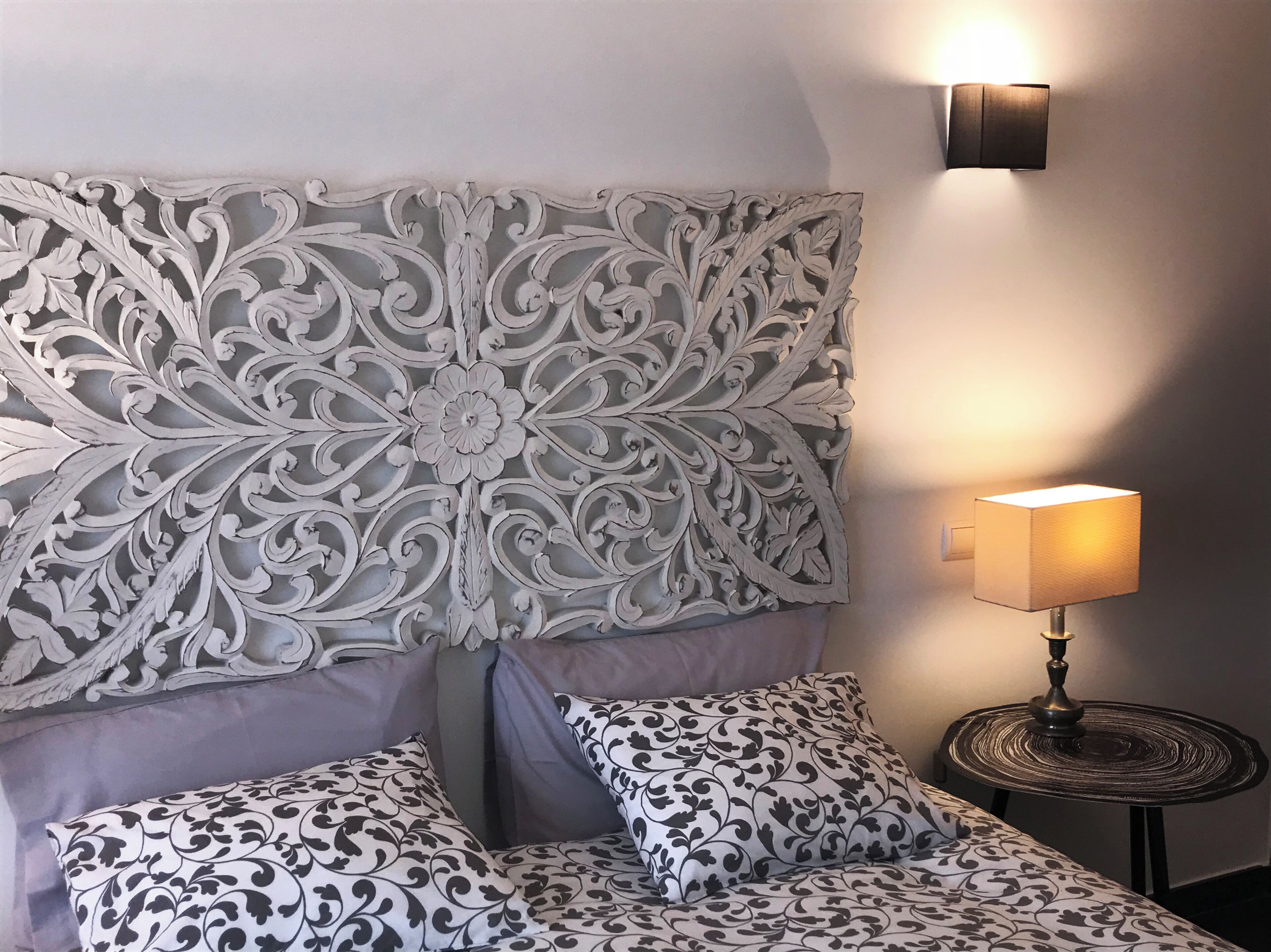 A bed with a decorative headboard, a bedside lamp, and patterned pillows.