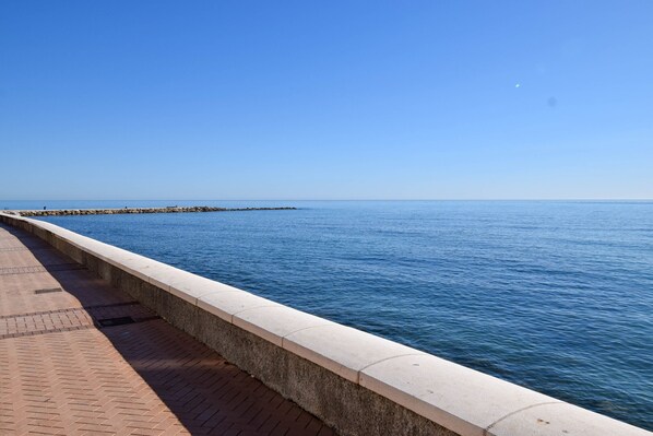 Un paseo marítimo con una pasarela de concreto y un muelle de piedra que se adentra en el agua.