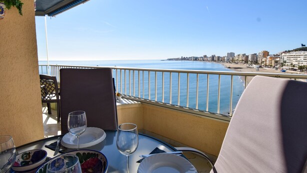 En balkon med et bord dækket til to, med udsigt over en strand og bybillede.