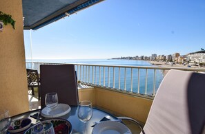 Un balcón con una mesa dispuesta para dos personas, con vista a la playa y al paisaje urbano.