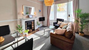Ein modernes Wohnzimmer mit Kamin, bequemen Sitzmöglichkeiten, einem Glastisch und einem großen Fenster mit Vorhängen.