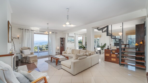 Amplia sala de estar con un sofá grande, una butaca y una mesa de centro. Se observa una escalera con barandilla de madera y vistas al exterior.