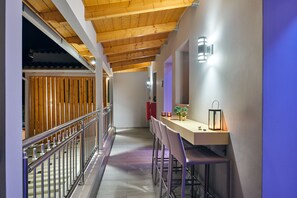 Un corridoio con soffitto in legno, una ringhiera, un'area bar con sgabelli e un fiorale a parete.