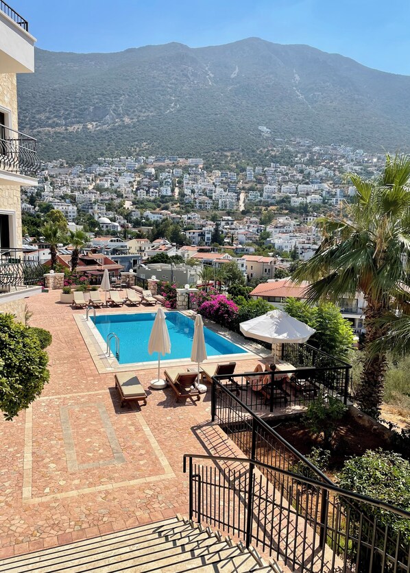 A pool area with lounge chairs and umbrellas, surrounded by a stone-tiled patio.