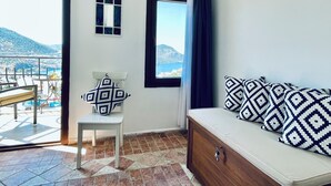 A room with a bed, a chair, a small table, and a view of the sea and mountains. - Kalkan Duplex Apartment - prime location with stunning views (Kalkan)