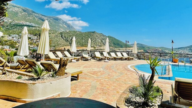 A poolside area with lounge chairs and umbrellas, a tiled deck, and a view of mountains in the background. - Kalkan Duplex Apartment - prime location with stunning views (Kalkan)