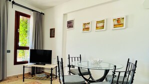 A dining area with a round glass table, four chairs, a television, and a window with curtains. - Kalkan Duplex Apartment - prime location with stunning views (Kalkan)