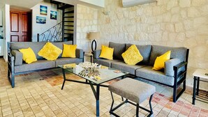 A living room with a grey sofa, yellow cushions, a glass coffee table, and a stone wall. - Kalkan Duplex Apartment - prime location with stunning views (Kalkan)