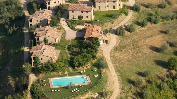 An aerial view of a residential area with multiple stone buildings, a swimming pool, and surrounding greenery. - Two-bedroom apartment with private entrance (Città della Pieve)