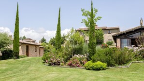 A stone house with a tiled roof, surrounded by a well-maintained lawn and various flowering plants. - Two-bedroom apartment with private entrance (Città della Pieve)