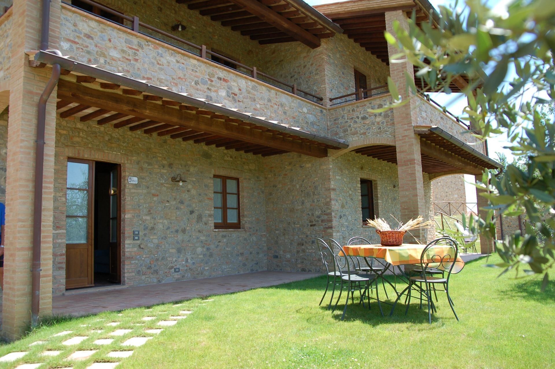 A stone building with a balcony, a table with chairs, and a grassy lawn.