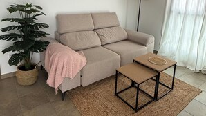 Un salon avec un canapé beige, une table basse, une plante en pot et deux œuvres d’art murales.