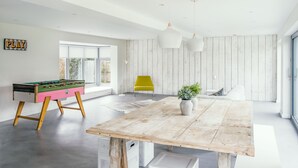 Ein modernes Wohnzimmer mit einem Kicker, einem Holzesstisch und einem leuchtend gelben Stuhl.