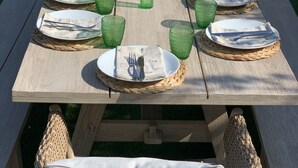 Ein Holztisch mit Picknick-Ausstattung, darunter Teller, Besteck und grünes Glas, umgeben von Korbstühlen.