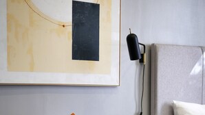 A modern living room with a grey armchair, an orange pillow, a small black table, and a wall-mounted lamp.