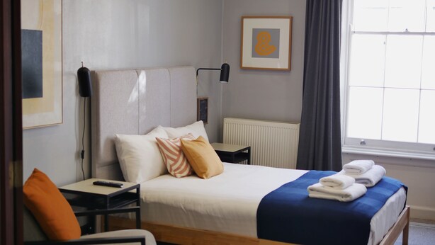A neatly arranged hotel room with a bed, a bedside table, a chair, a desk, and a window with curtains.