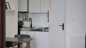 A compact kitchen with white cabinets, a stove, a sink, and a dining area with a table and chairs.