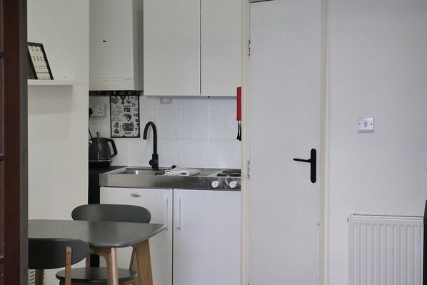 Cocina compacta con armarios blancos, estufa, pileta y comedor con mesa y sillas.