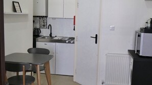 A compact kitchen with white cabinets, a dining table with chairs, a clock on the wall, and a radiator.