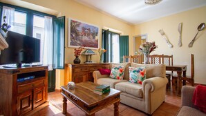Een woonkamer met een televisie, bank, salontafel en een eethoek met stoelen en een tafel.