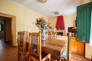 Un comedor con una mesa y sillas de madera, un jarrón con flores y una pared roja.