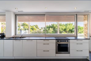 A modern kitchen with a large window, built-in oven, and white cabinetry.