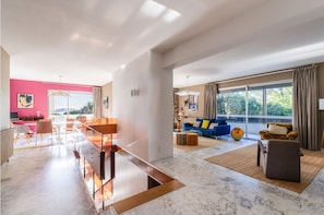 A spacious living area with a large window, a blue sofa, and a dining area with a long table.