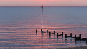 A calm sea at sunset with a solitary lamp post and wooden posts in the water. - Holly Lodge, Cedar Springs, Heacham. 5 Mins Walk to Beach (Heacham)
