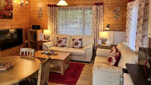 A cozy cabin-style room with a wooden interior, a sofa set, a dining table, and a TV. - Holly Lodge, Cedar Springs, Heacham. 5 Mins Walk to Beach (Heacham)