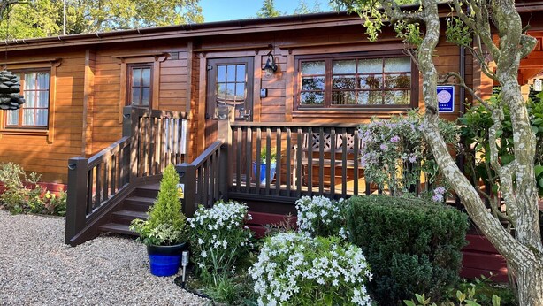 A wooden building with a porch, a staircase, and a sign indicating self-catering facilities. - Holly Lodge, Cedar Springs, Heacham. 5 Mins Walk to Beach (Heacham)
