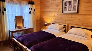 A wooden cabin room with two beds, a nightstand, a lamp, and a framed floral artwork on the wall. - Holly Lodge, Cedar Springs, Heacham. 5 Mins Walk to Beach (Heacham)