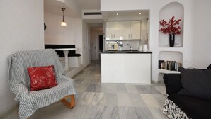 A modern living room with a checkered armchair, a black sofa, and a kitchen area with white cabinets and a central island.