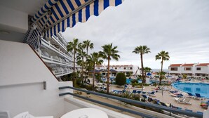 A balcony with a view of a pool area, palm trees, and a cruise ship deck.