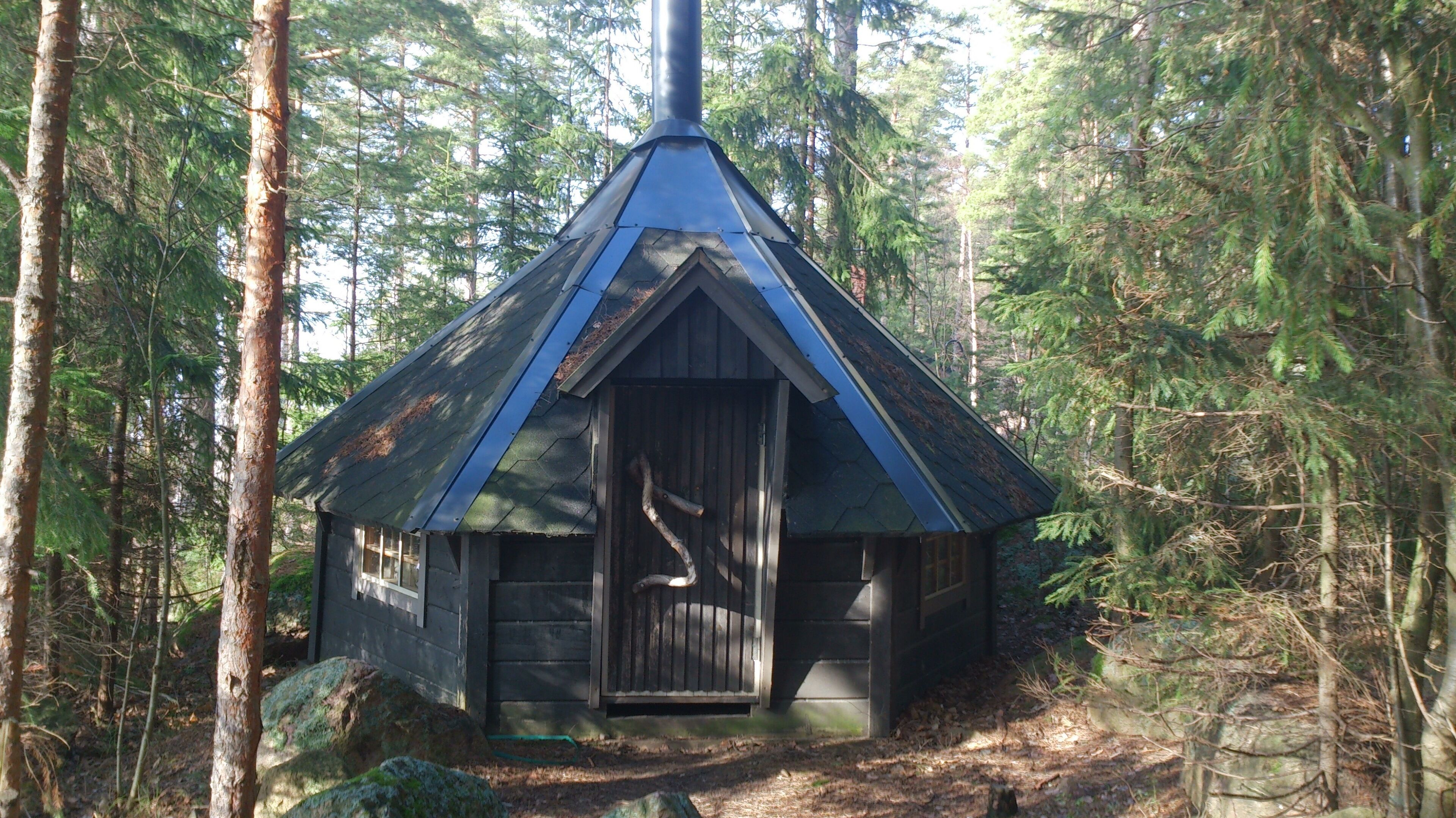 Pieni mökki, jonka katto on erittäin jyrkkä, ja jonka ympärillä on tiheä metsä.